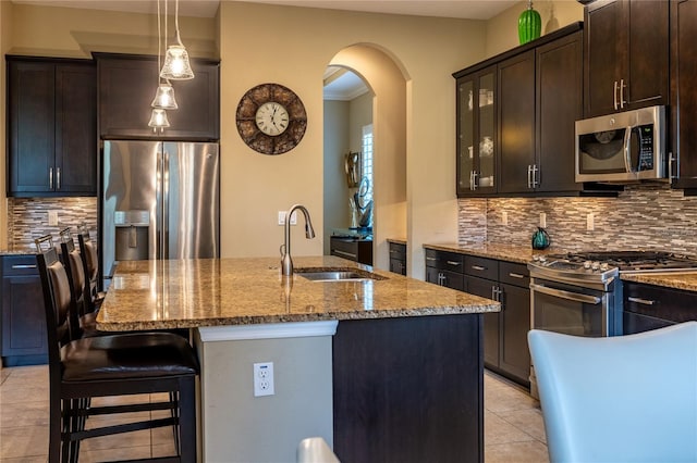 kitchen featuring stone counters, stainless steel appliances, a breakfast bar, a sink, and tasteful backsplash