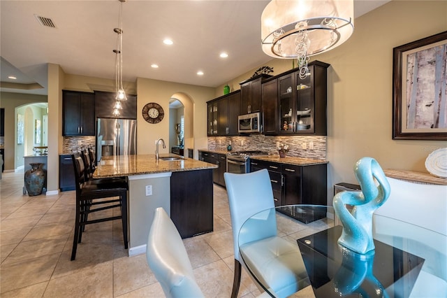 kitchen featuring arched walkways, decorative backsplash, light stone counters, stainless steel appliances, and a sink