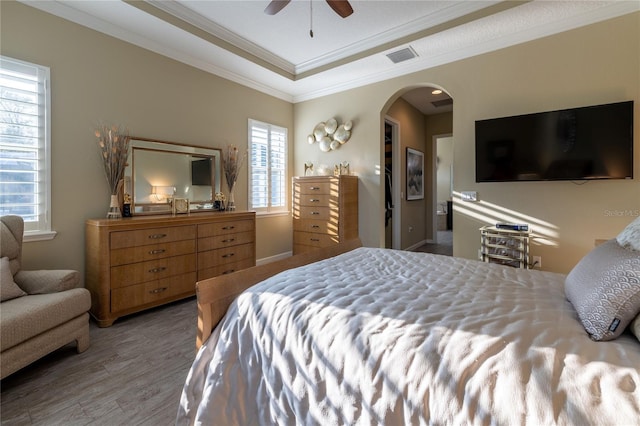 bedroom with arched walkways, wood finished floors, visible vents, a ceiling fan, and ornamental molding