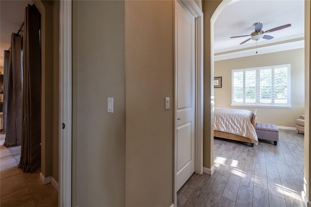 hall with baseboards, arched walkways, crown molding, and wood finished floors