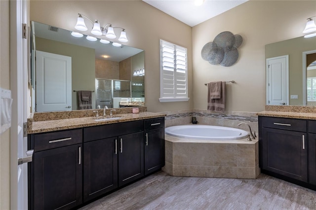 bathroom with a garden tub, wood finished floors, two vanities, a sink, and a stall shower