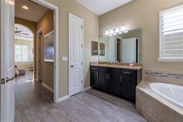 bathroom with baseboards, a ceiling fan, wood finished floors, a garden tub, and vanity