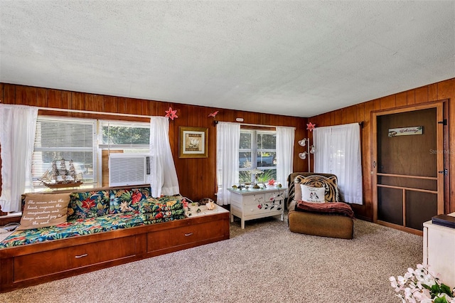 living area featuring a healthy amount of sunlight, wooden walls, carpet flooring, and a textured ceiling