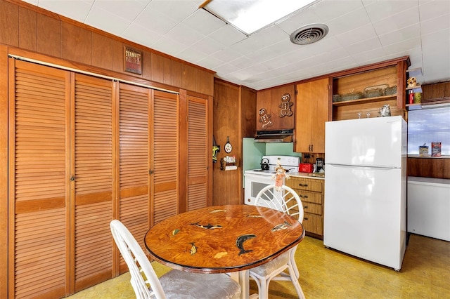 kitchen with under cabinet range hood, white appliances, wood walls, visible vents, and light floors