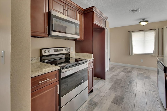 kitchen featuring light stone counters, stainless steel appliances, visible vents, light wood-style floors, and a textured ceiling