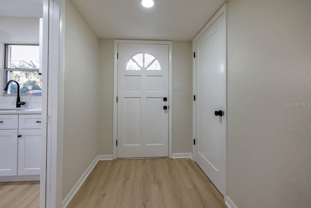 entryway with light wood-type flooring, baseboards, and a sink