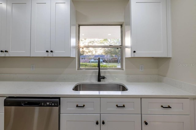 kitchen with stainless steel dishwasher, a sink, light stone countertops, and white cabinets