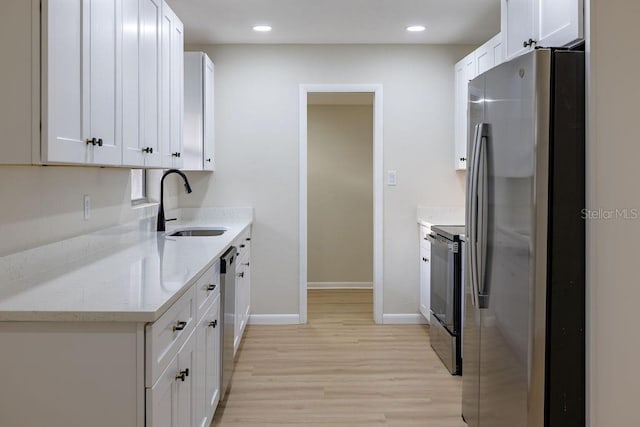 kitchen with appliances with stainless steel finishes, light wood-style floors, white cabinets, a sink, and light stone countertops