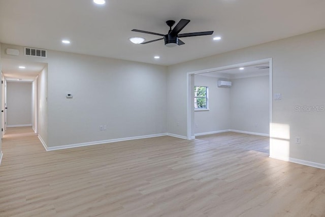 empty room featuring a wall unit AC, light wood finished floors, visible vents, and a ceiling fan