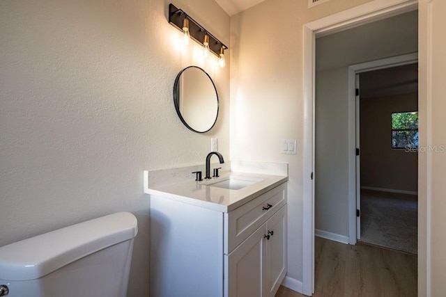 half bathroom with toilet, baseboards, wood finished floors, and vanity