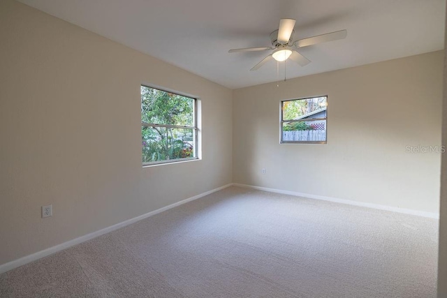 carpeted spare room featuring a ceiling fan, plenty of natural light, and baseboards