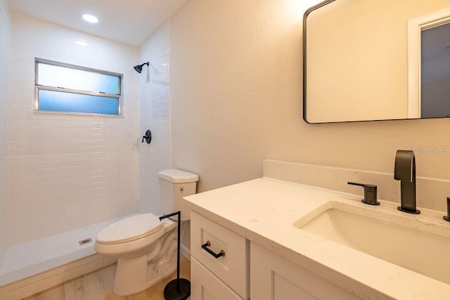 bathroom featuring recessed lighting, toilet, vanity, wood finished floors, and tiled shower