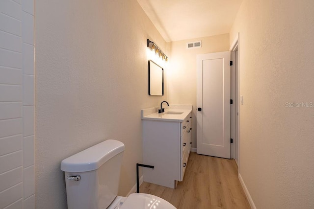 half bathroom with toilet, wood finished floors, vanity, visible vents, and baseboards