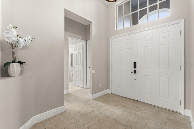 foyer with light tile patterned flooring, a towering ceiling, and baseboards