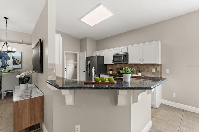 kitchen with a peninsula, a breakfast bar, white cabinetry, appliances with stainless steel finishes, and tasteful backsplash