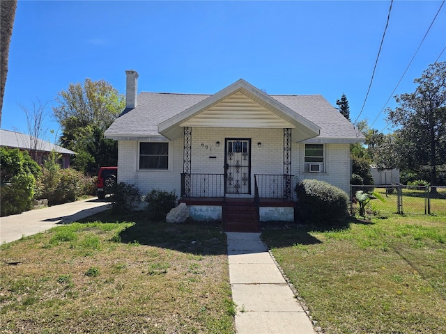 bungalow with brick siding, a chimney, a porch, a front yard, and fence