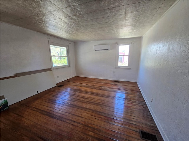 spare room with a textured wall, visible vents, baseboards, an AC wall unit, and wood-type flooring