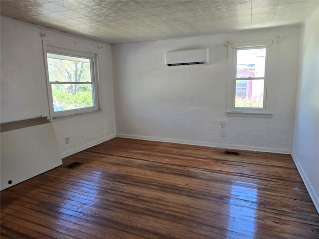 unfurnished room featuring wood-type flooring, a wall unit AC, visible vents, and baseboards