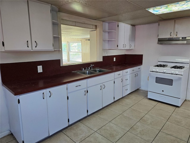 kitchen with under cabinet range hood, white range with gas stovetop, a sink, open shelves, and dark countertops