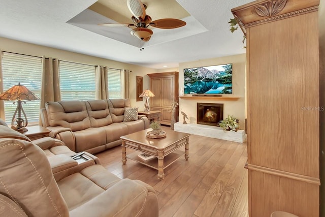 living room with light wood finished floors, plenty of natural light, a raised ceiling, and a glass covered fireplace