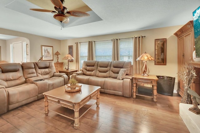 living room with light wood-style floors, a ceiling fan, a tray ceiling, and a textured ceiling