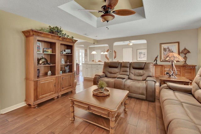 living area featuring baseboards, a raised ceiling, a ceiling fan, and light wood-style floors