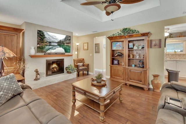 living room with a tray ceiling, a glass covered fireplace, ceiling fan, and hardwood / wood-style flooring