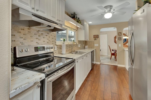 kitchen with stainless steel appliances, wood-type flooring, white cabinetry, a sink, and under cabinet range hood