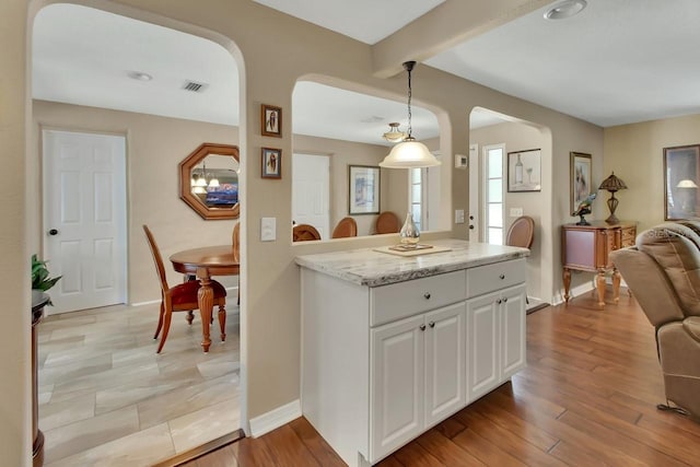 kitchen with open floor plan, arched walkways, white cabinetry, and light wood-style floors