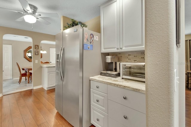 kitchen featuring light wood-style floors, arched walkways, stainless steel fridge, and white cabinetry