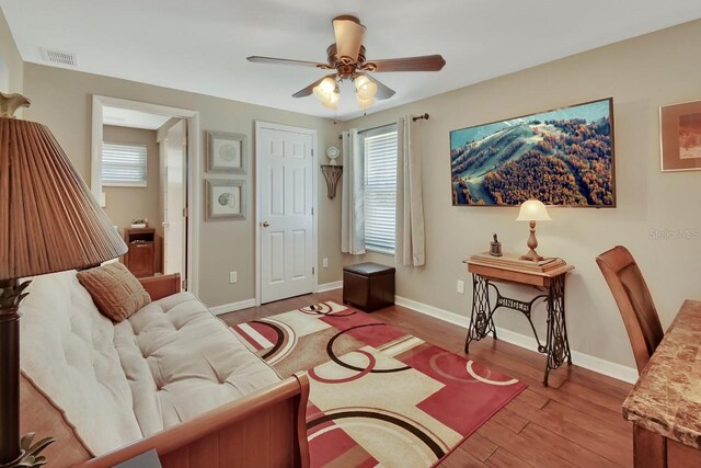 living room featuring ceiling fan, visible vents, plenty of natural light, and wood finished floors