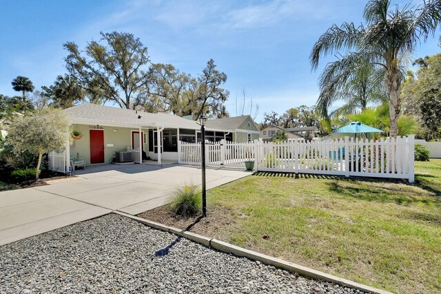 view of front facade featuring concrete driveway, a sunroom, a fenced front yard, central AC, and a front yard