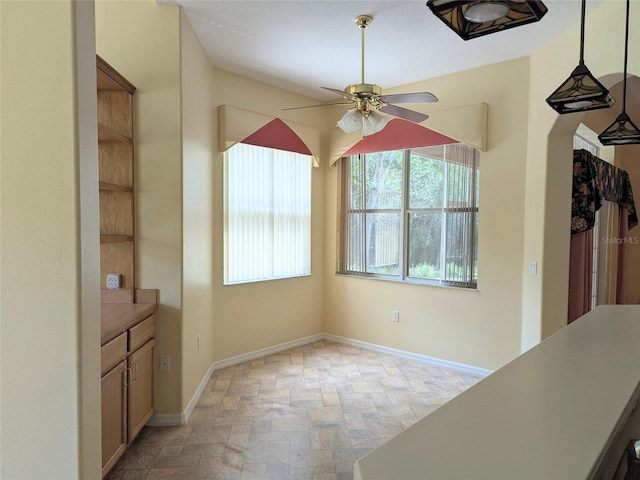 unfurnished dining area with baseboards, a ceiling fan, and stone finish flooring