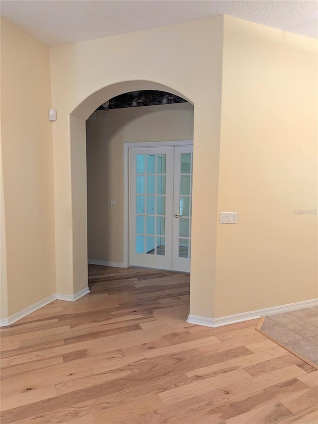 hallway with arched walkways, light wood-style floors, french doors, and baseboards