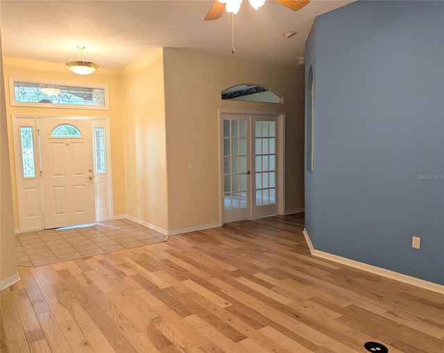 foyer entrance featuring french doors, baseboards, light wood finished floors, ceiling fan, and arched walkways