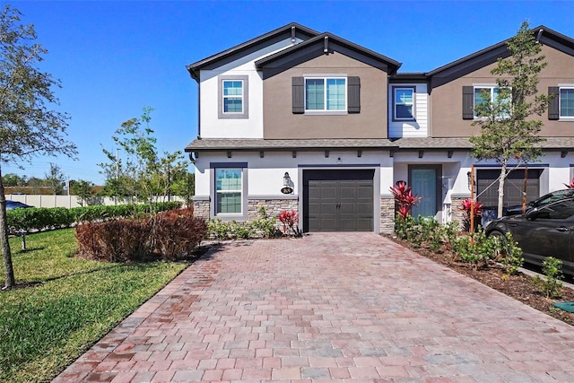 craftsman-style house with stucco siding, a front lawn, a garage, stone siding, and decorative driveway