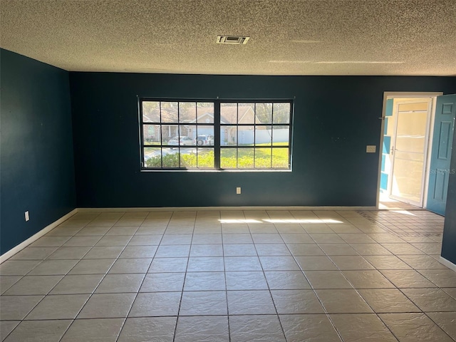 tiled empty room with baseboards, visible vents, and a textured ceiling