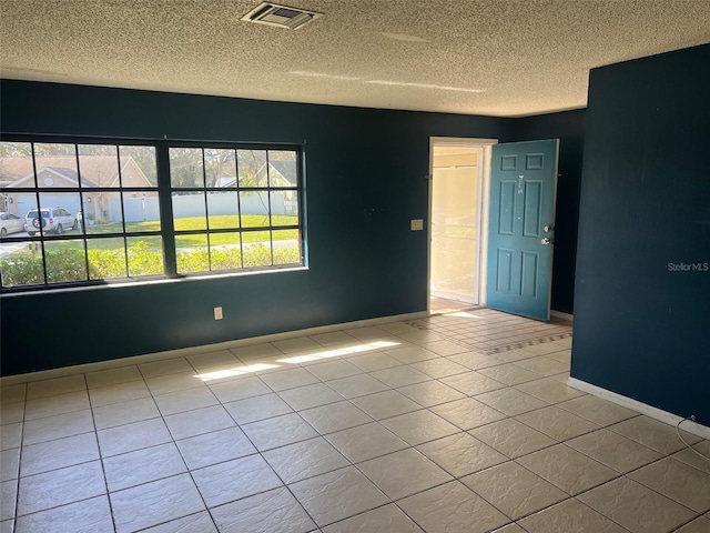 tiled empty room with visible vents, a textured ceiling, and baseboards