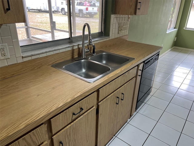 kitchen with black dishwasher, a sink, light countertops, backsplash, and light tile patterned flooring