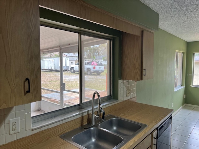 kitchen with a textured ceiling, dishwashing machine, light tile patterned floors, a sink, and baseboards