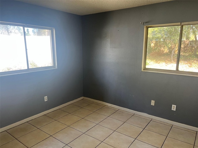 empty room featuring a textured ceiling, light tile patterned flooring, and baseboards