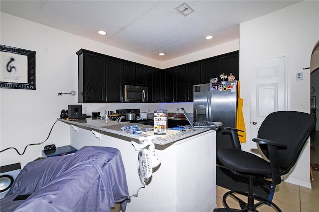 kitchen with light tile patterned floors, a breakfast bar area, dark cabinets, stainless steel appliances, and a peninsula