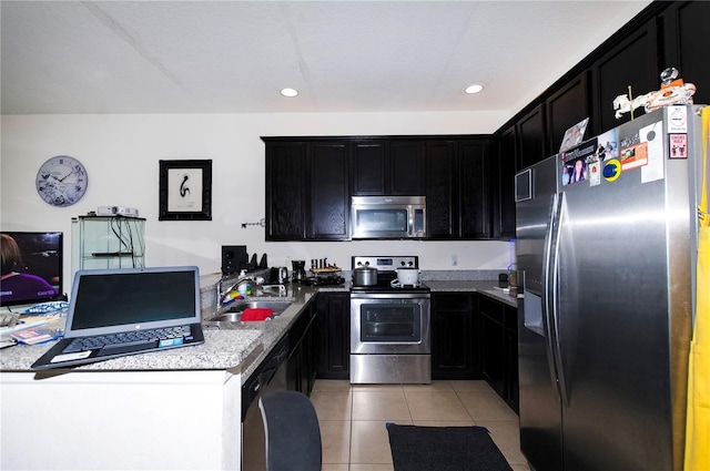 kitchen featuring light tile patterned floors, appliances with stainless steel finishes, dark cabinets, a sink, and recessed lighting