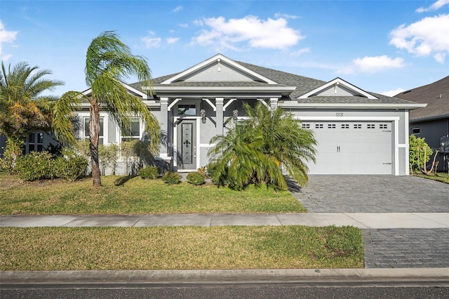 view of front facade with a front lawn, roof with shingles, stucco siding, decorative driveway, and a garage