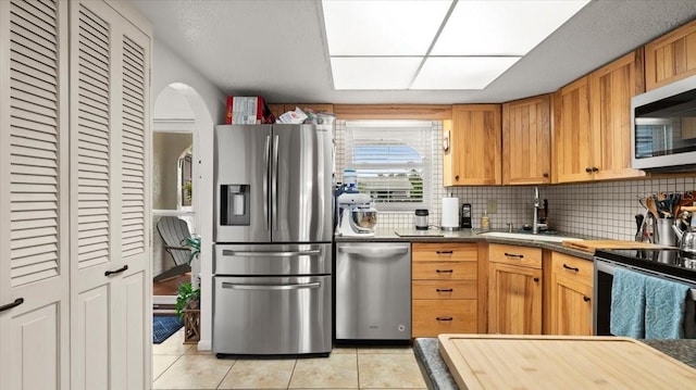 kitchen featuring stainless steel appliances, backsplash, light tile patterned flooring, and a sink