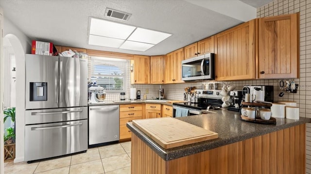 kitchen with a peninsula, visible vents, stainless steel appliances, and backsplash