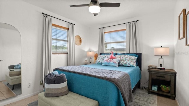 tiled bedroom with ceiling fan, multiple windows, arched walkways, and baseboards