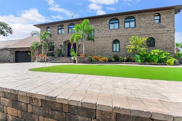 view of front of house with decorative driveway, a front lawn, an attached garage, and brick siding