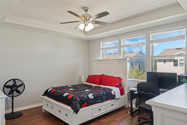 bedroom with baseboards, multiple windows, a tray ceiling, and dark wood-type flooring