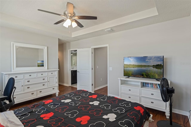 bedroom featuring a tray ceiling, dark wood-type flooring, and baseboards